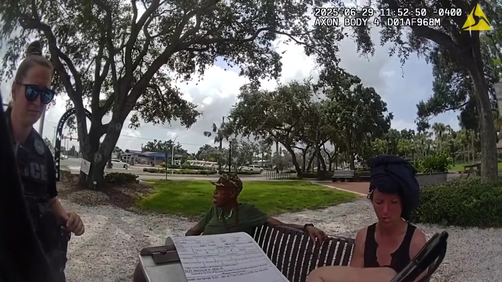 Officer completing paperwork beside people seated at the park bench