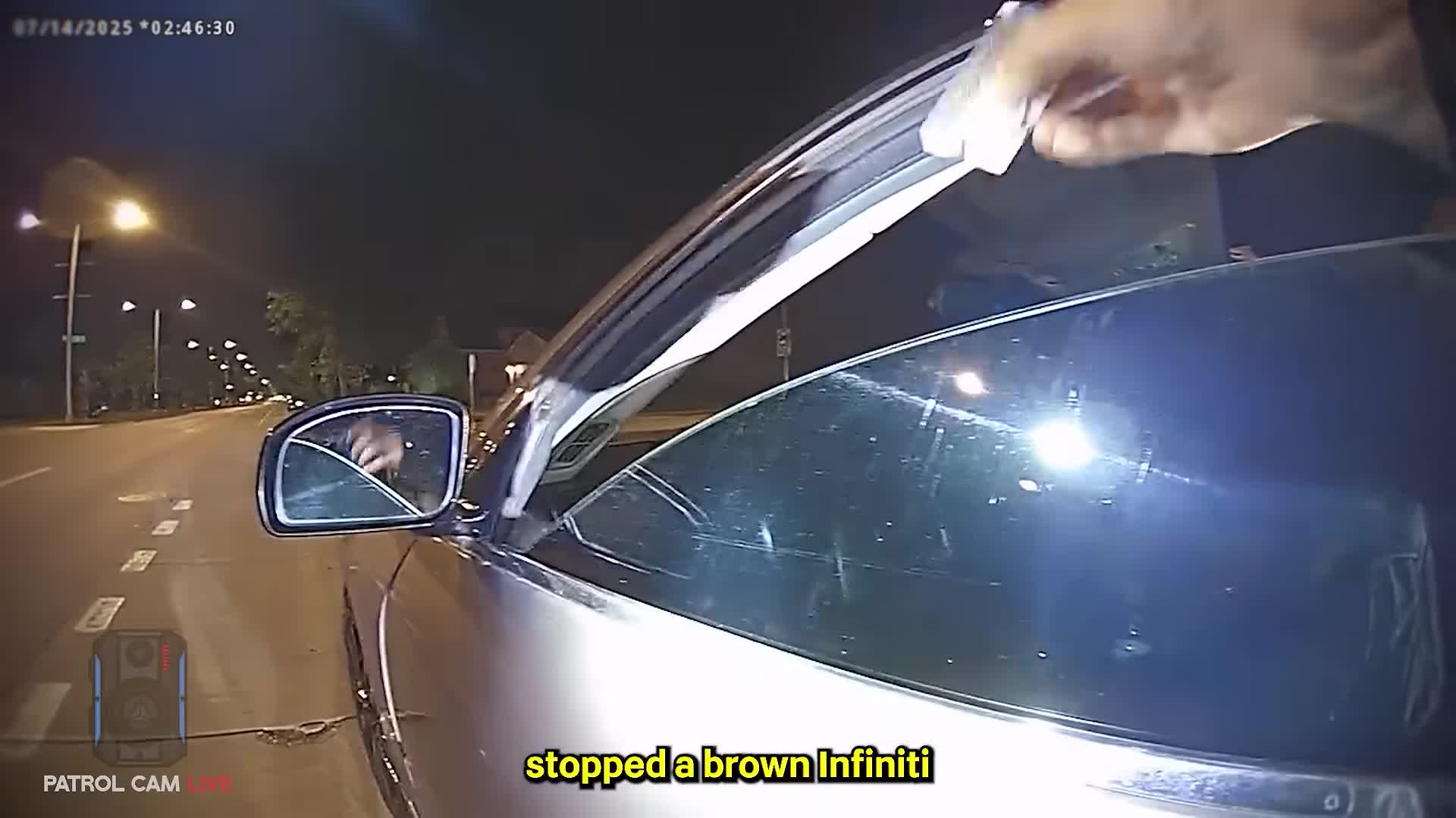 Body-camera frame showing a Greenwood police officer at the brown Infiniti during the July 14, 2025 traffic stop