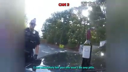 Body-camera frame showing an officer documenting a wine bottle after the traffic stop